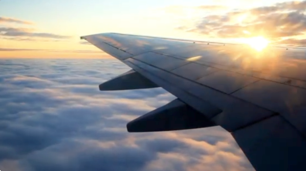 image of a window side passenger view looking at the airplane wing and sunset